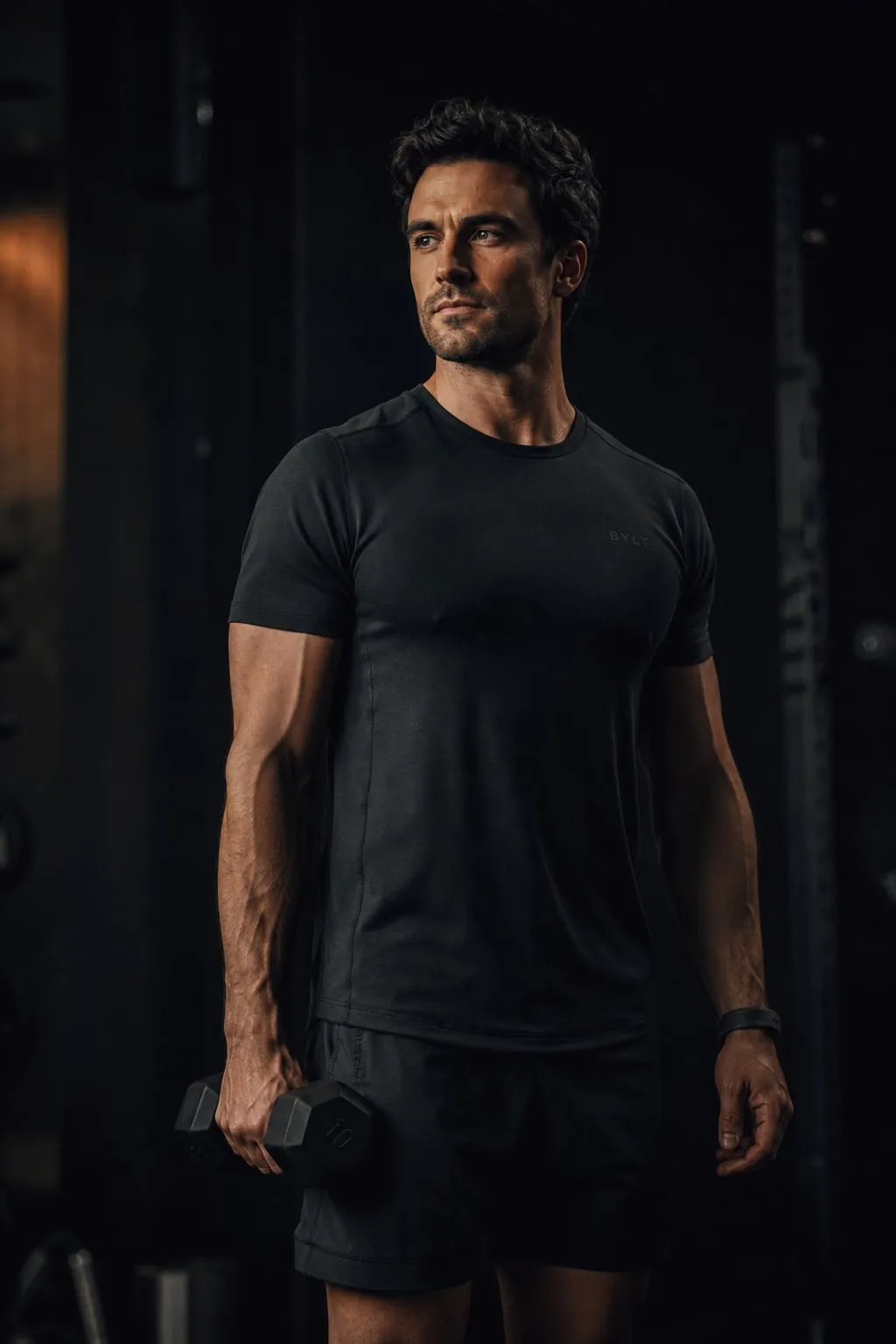 A beginner standing calmly in a quiet gym, one light dumbbell held loosely in one hand at his side